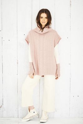 A woman is wearing a pale pink knitted poncho and matching wristwarmers.