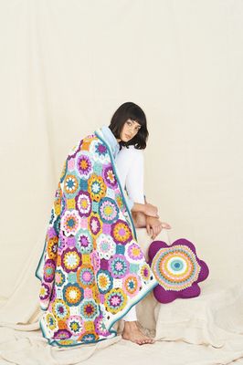 A woman is wearing a crocheted blanket made up of pink, purple, blue, orange and yellow flower shapes.
