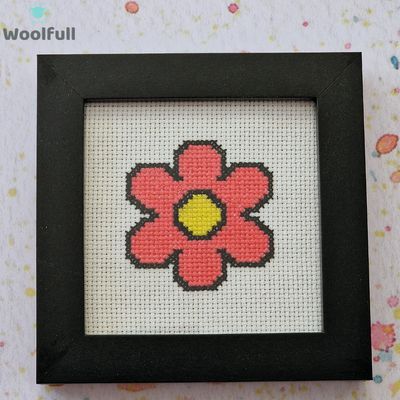 A framed cross stitch with a design of a pink cartoon style flower.