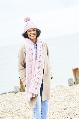 A woman is wearing a pink knitted hat and scarf set with lace detail.