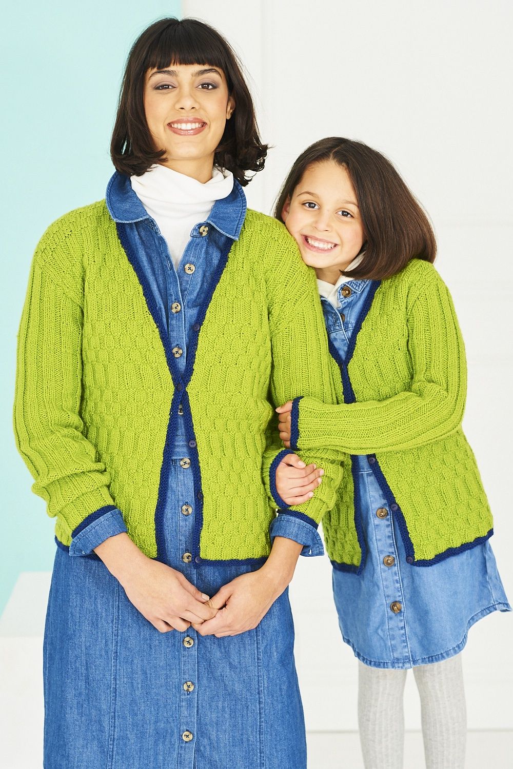 A woman and a girl are wearing matching green knitted cardigans with navy blue trim.