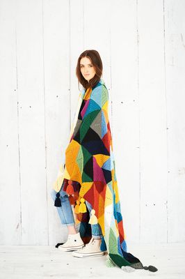 A woman has a crocheted blanket in shades of yellow, green, blue and red draped around her shoulders.