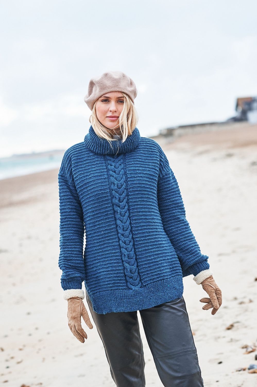 A woman is wearing a dark blue knitted sweater with a cable panel down the centre.