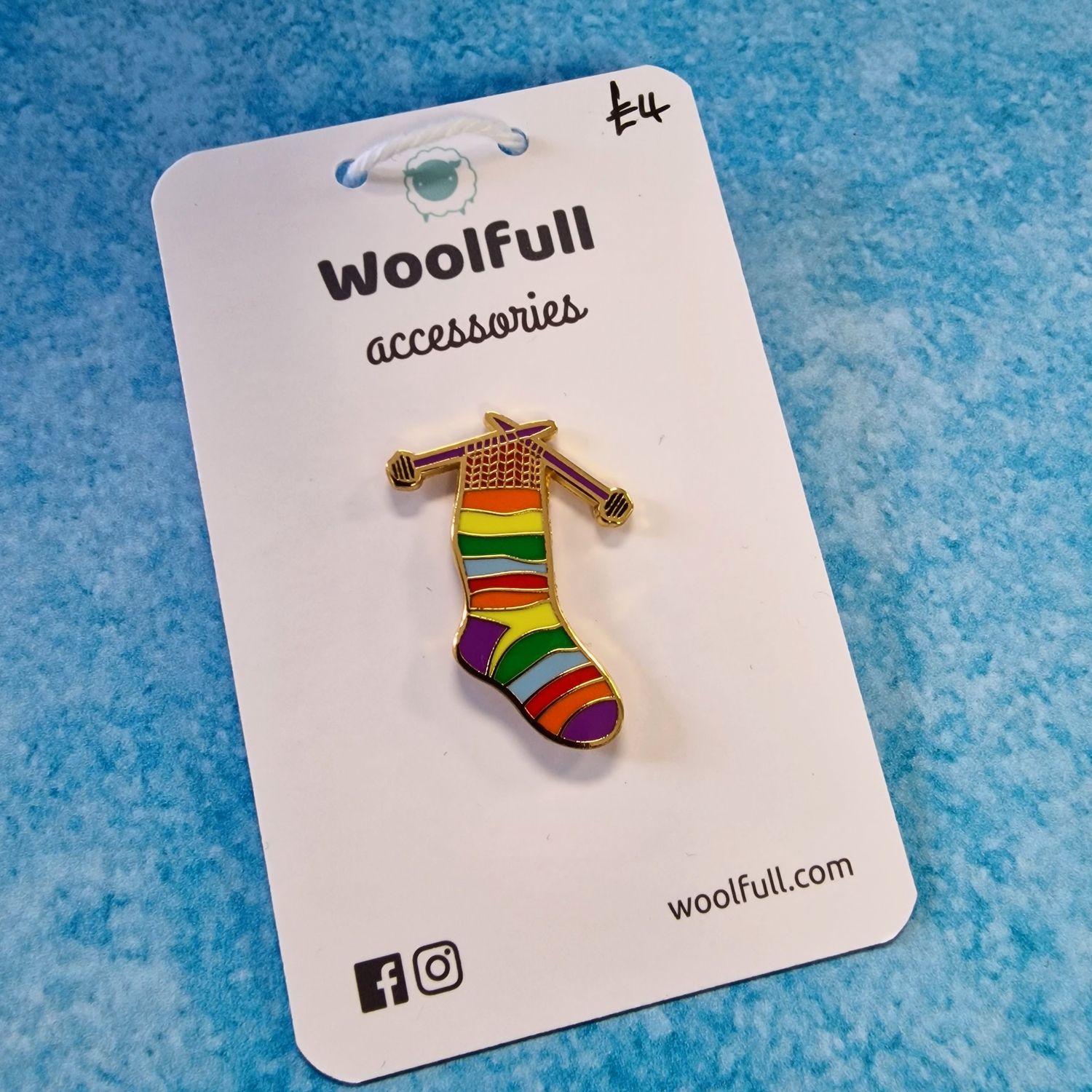 A blue background with a pin badge of a rainbow striped sock on knitting needles.