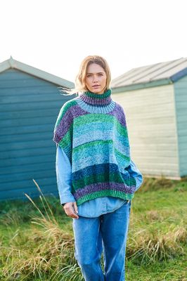 A woman is wearing a knitted poncho in shades of green, purple and blue.