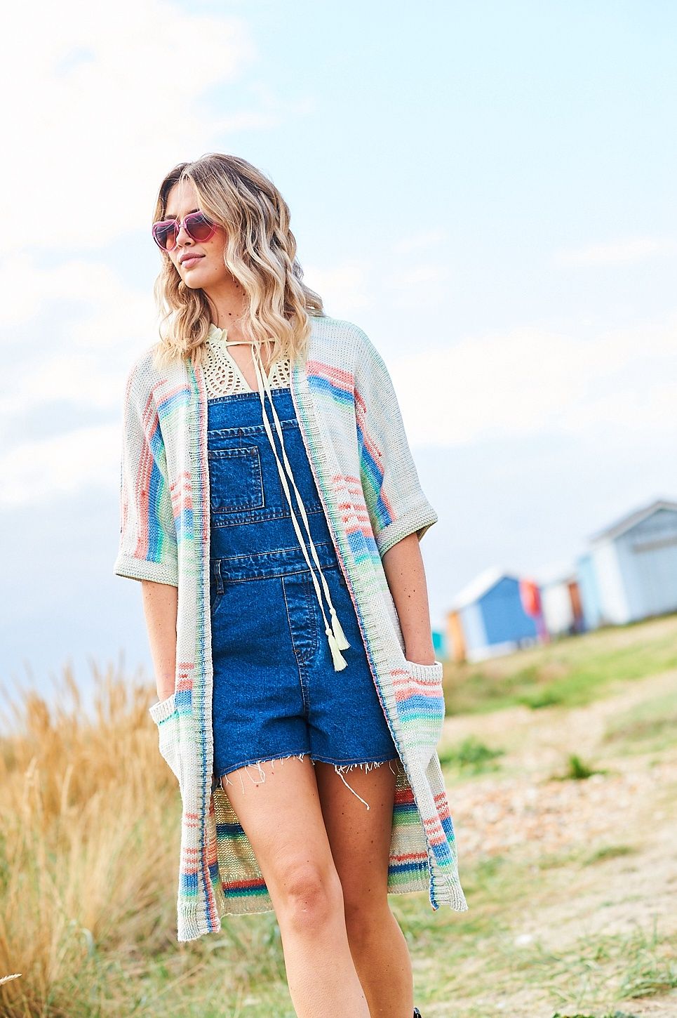 A woman is wearing a long knitted cardigan in shades of cream, blue, green and pink.