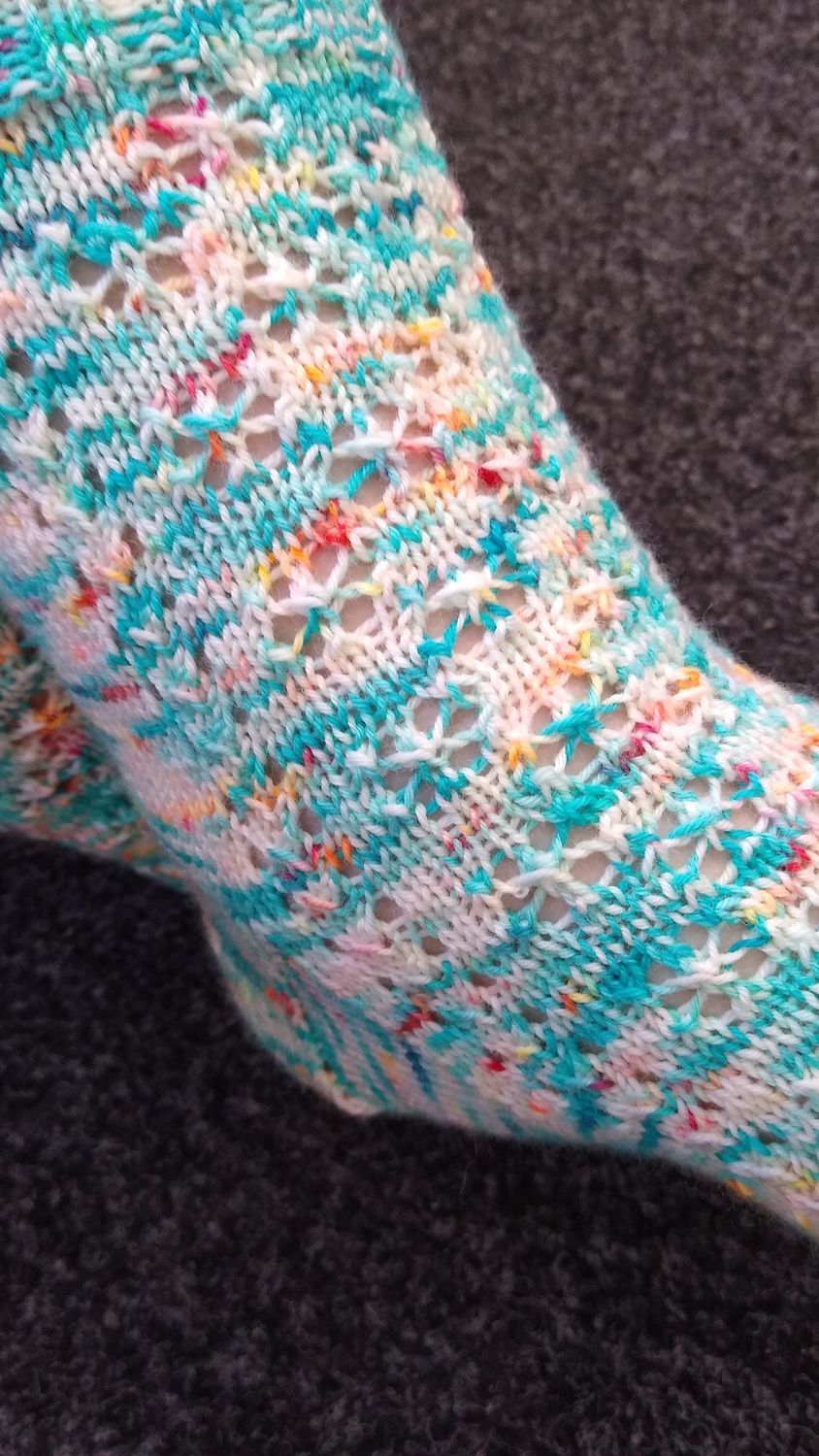 A knitted sock in blue, cream and orange yarn with lace detail.