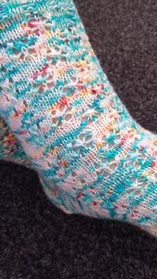 A knitted sock in blue, cream and orange yarn with lace detail.