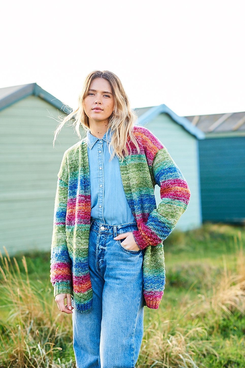 A woman is wearing a knitted cardigan in shades of red, blue and green.