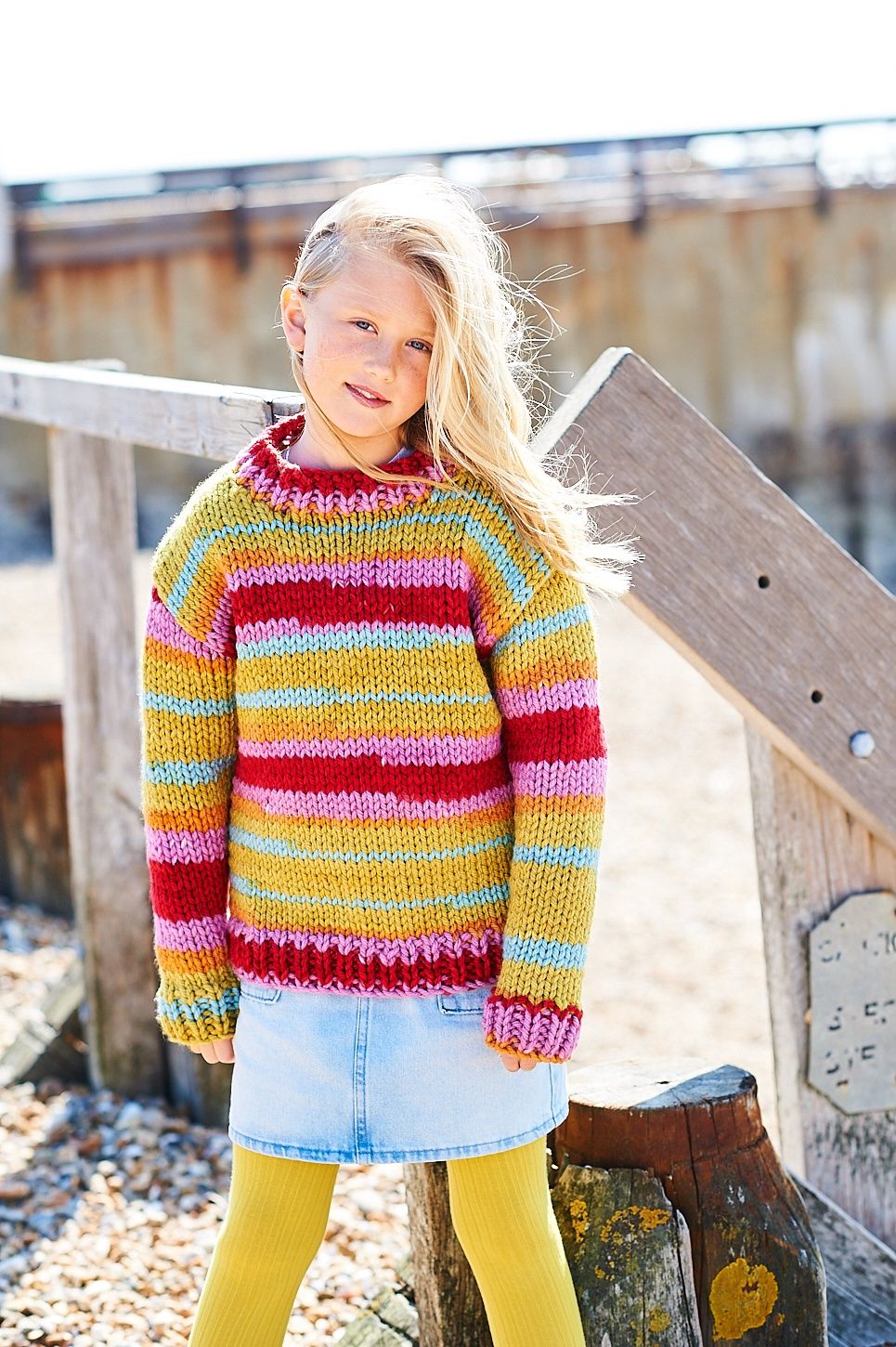 A girl is wearing a variegated knitted sweater in shades of blue, pink, red and green.