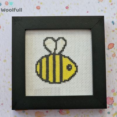 A framed cross stitch with a design of a cartoon style bee.
