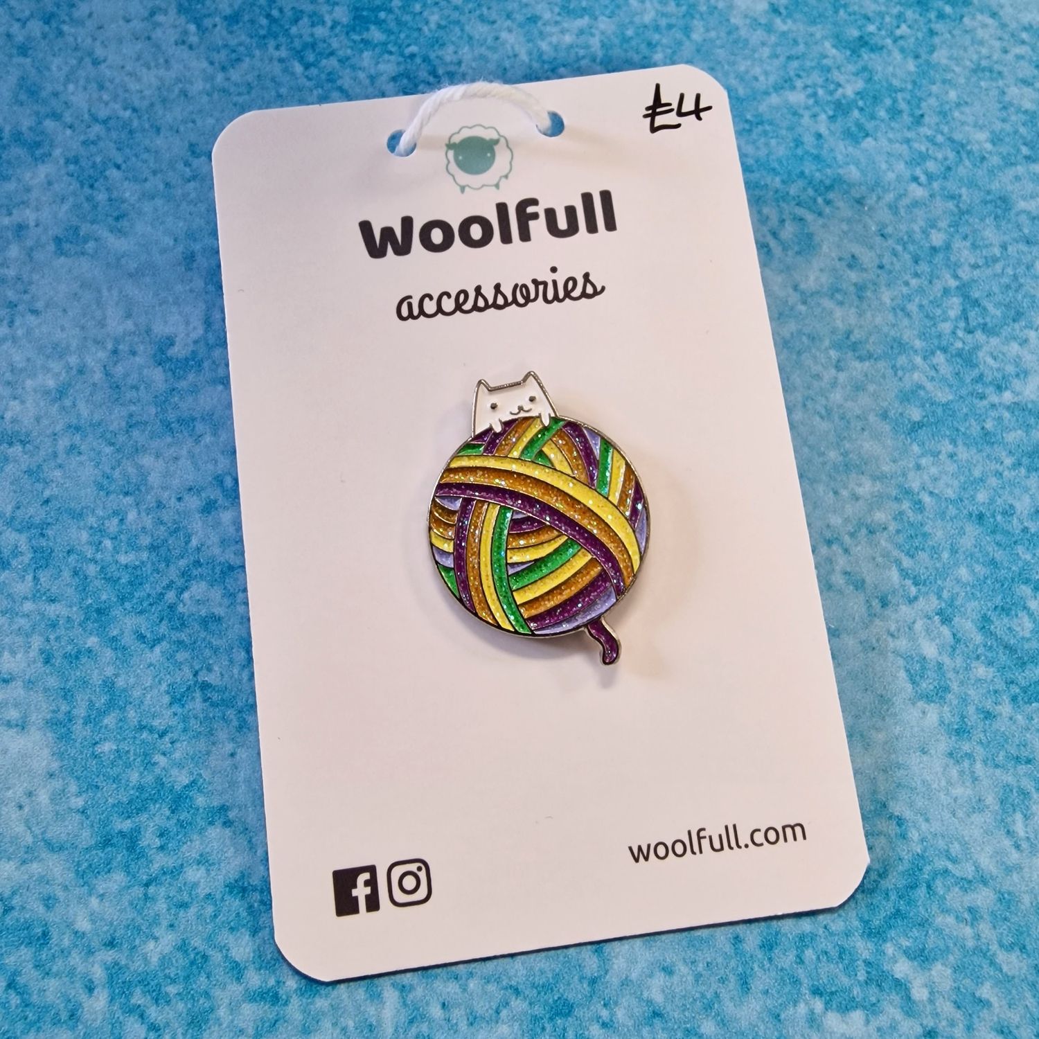 A blue background with a pin badge of a cat peeking out from behind a rainbow ball of yarn.