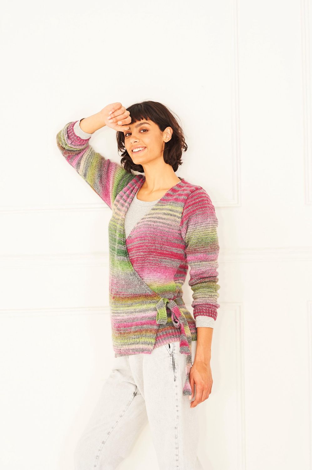 A woman is wearing a knitted cardigan in shades of grey, pink and green.
