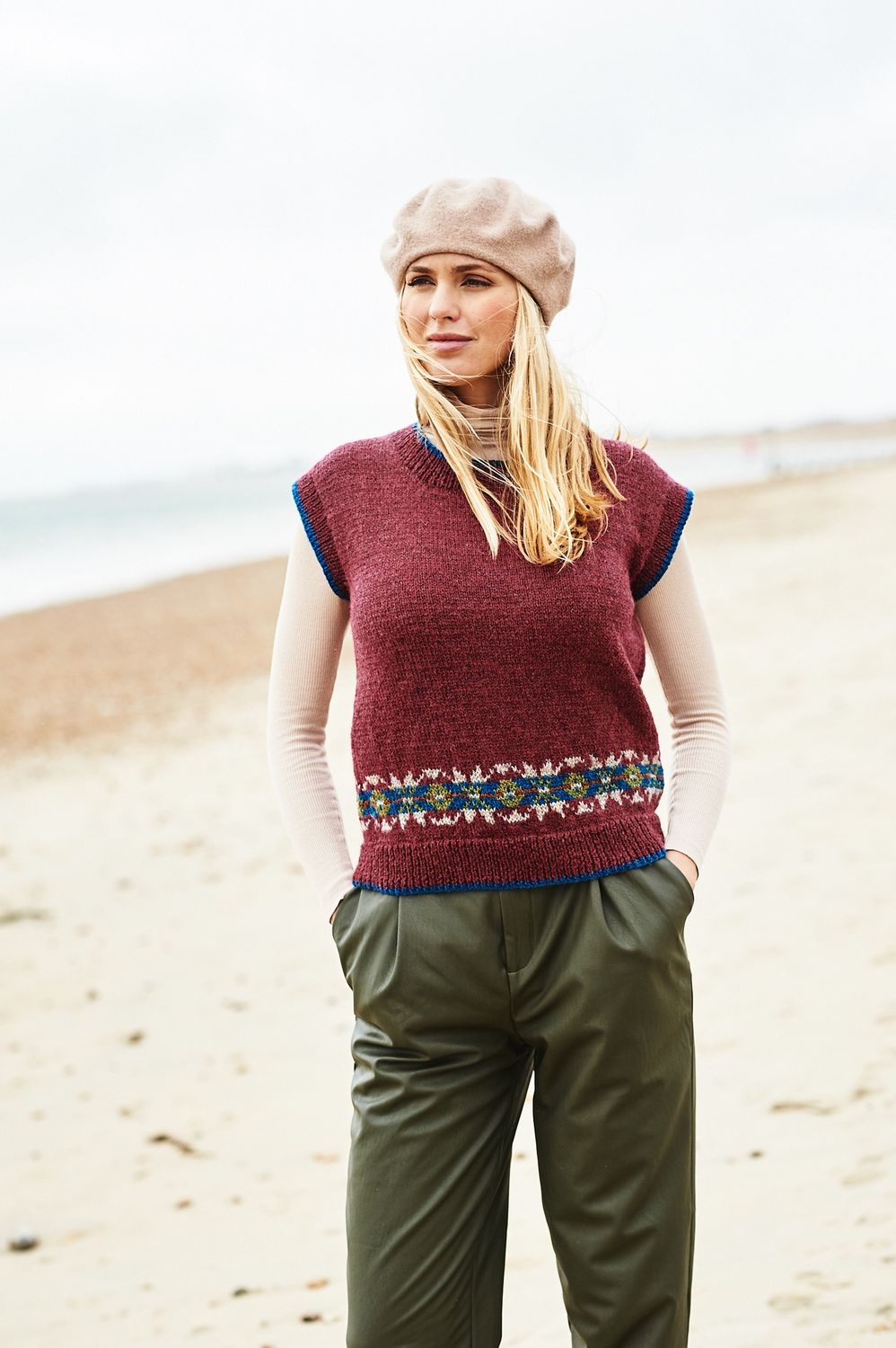 A woman is wearing a dark red knitted tank top with a small amount of fair isle around the bottom edge.