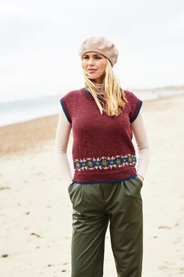 A woman is wearing a dark red knitted tank top with a small amount of fair isle around the bottom edge.