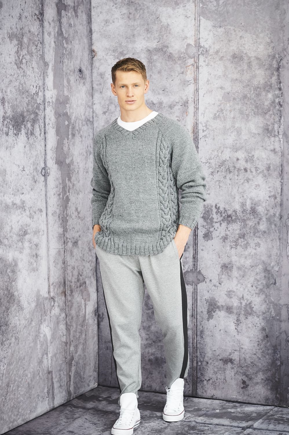 A man is wearing a grey knitted sweater with cable on the sides.