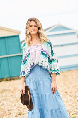 A woman is wearing a knitted wavy cardigan in shades of cream, green and purple.