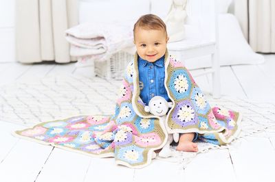 A baby is wrapped in a crocheted blanket made up oh pink, blue, purple and cream hexagons and joined together with green.