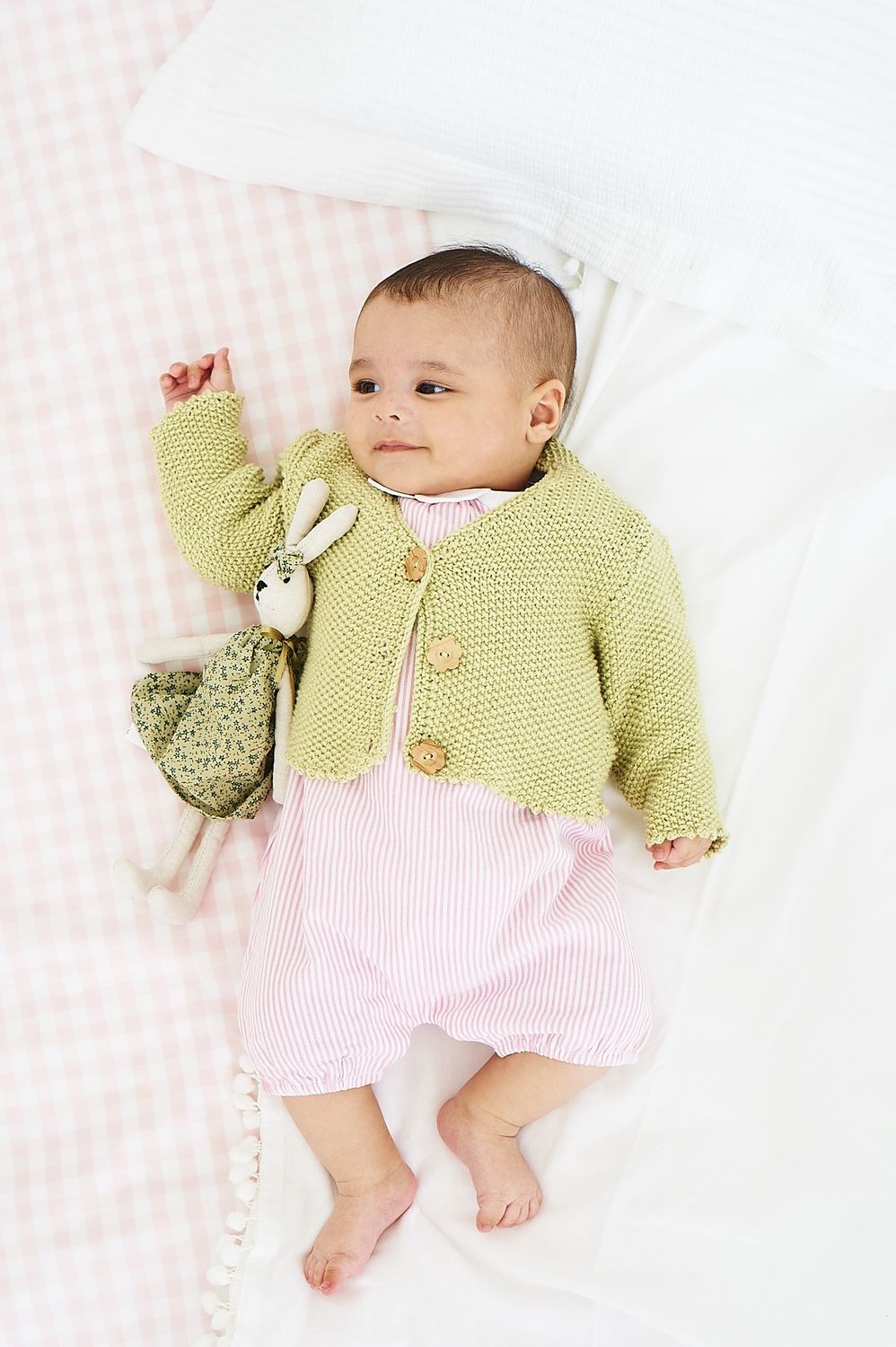A baby is wearing a pale green knitted cardigan.