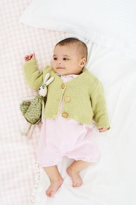 A baby is wearing a pale green knitted cardigan.