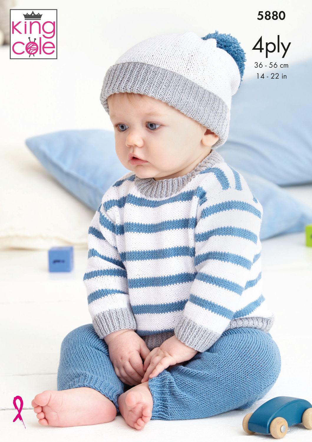 A baby is wearing a white, grey and blue sweater, blue trousers and a white, grey and blue hat.