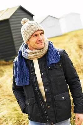 A man is wearing a cream hat and a cream and blue scarf.