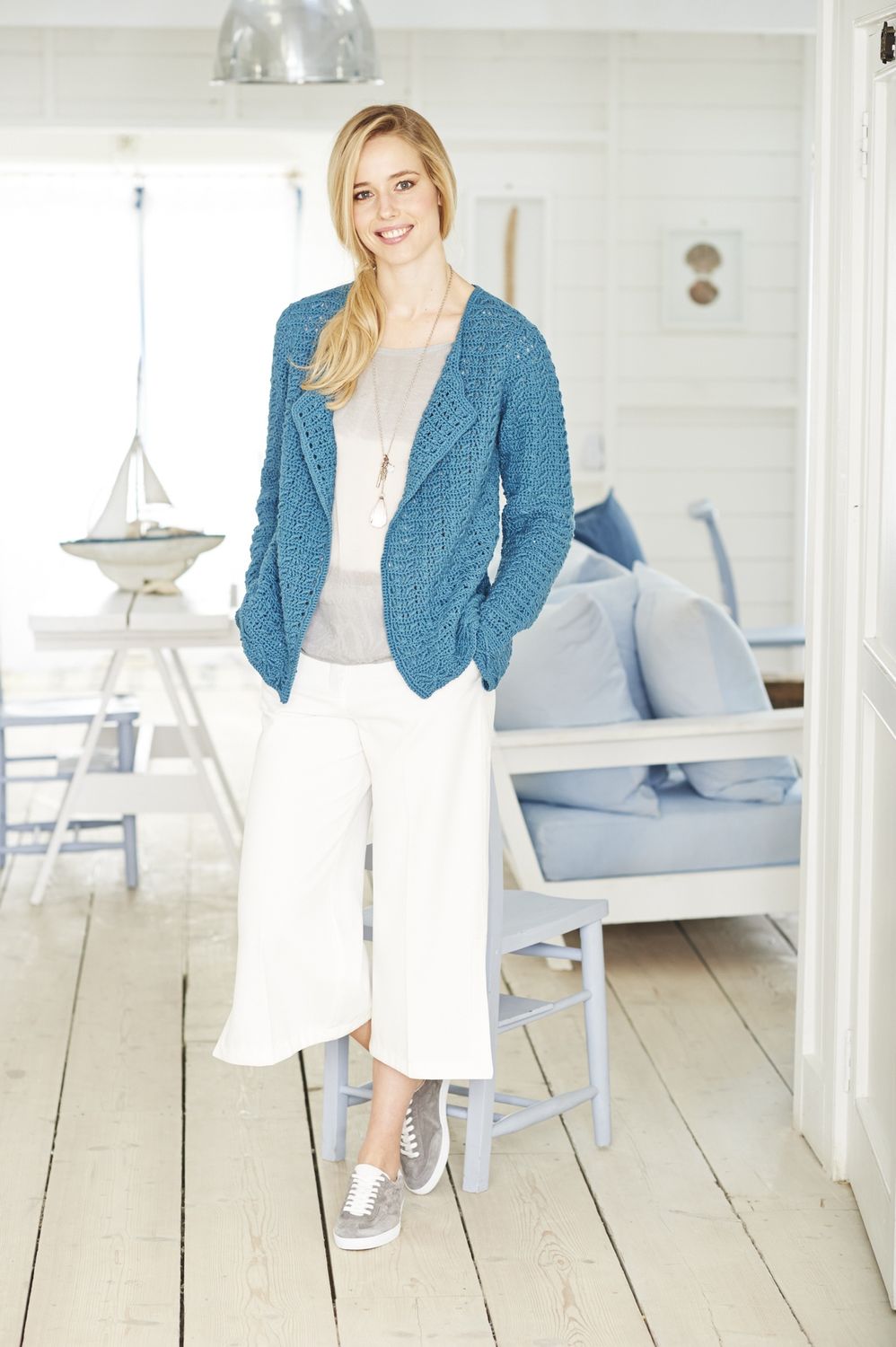 A woman is wearing a denim blue crocheted cardigan.