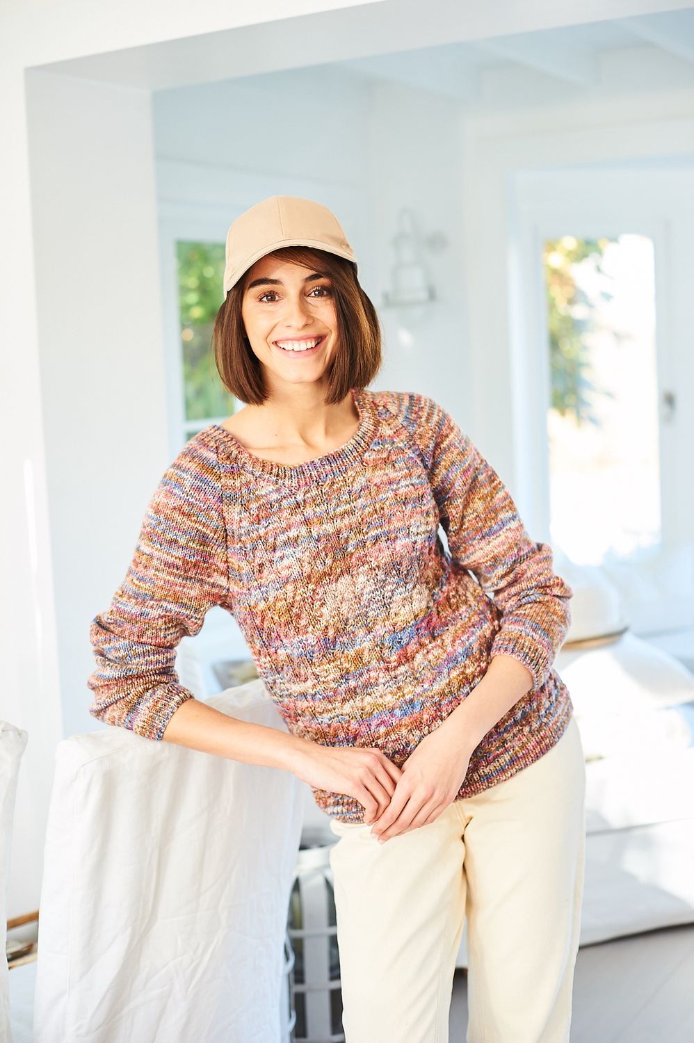 A woman is wearing a knitted sweater in a variegated brown, blue and red yarn.