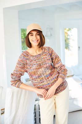 A woman is wearing a knitted sweater in a variegated brown, blue and red yarn.