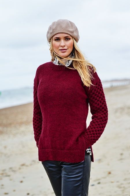 A woman on the beach is wearing a dark red sweater with a honeycomb pattern on the sleeves.