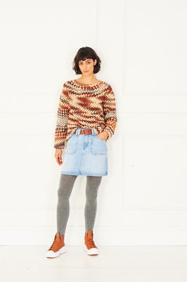 A woman is wearing a crocheted sweater in shades of cream, brown and red.