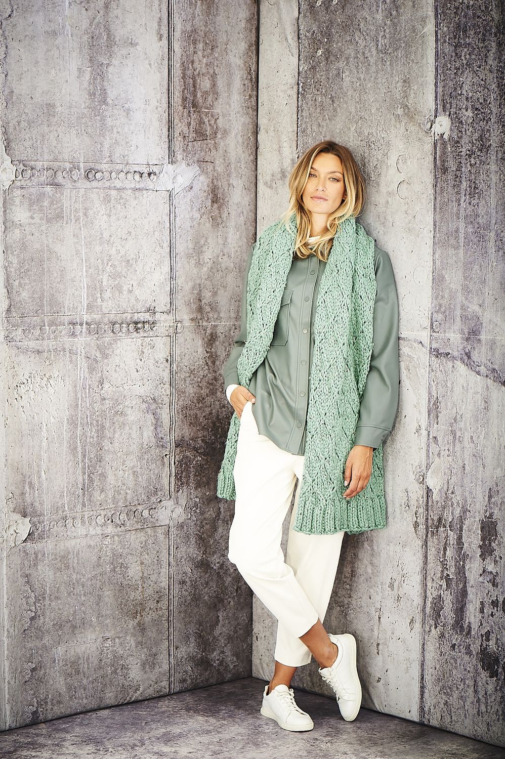 A woman is wearing a sage green knitted scarf.