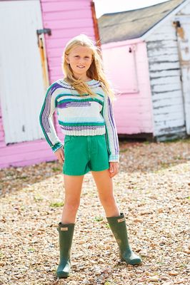 A girl is wearing a knitted sweater in shades of cream, green, blue and purple.