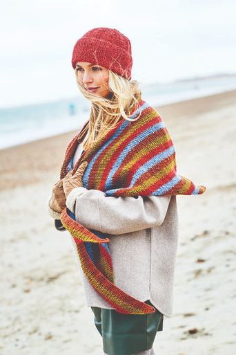 A woman is wearing a red knitted hat and a red, blue, brown and green striped knitted shawl.