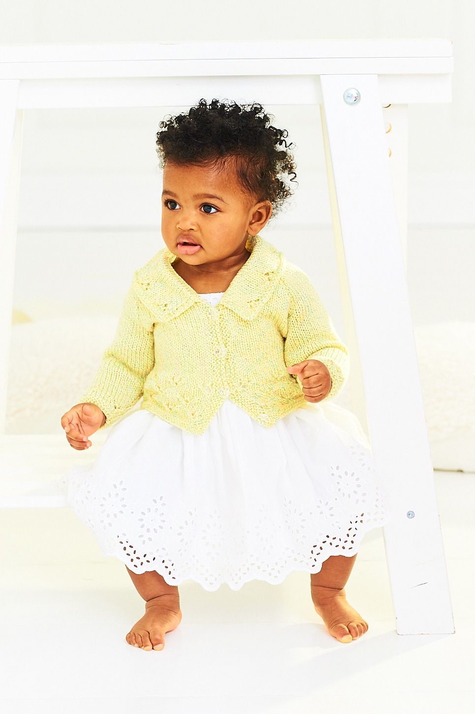 A baby is wearing a knitted yellow cardigan.