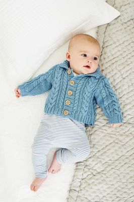 A baby is wearing a blue cable knit cardigan.
