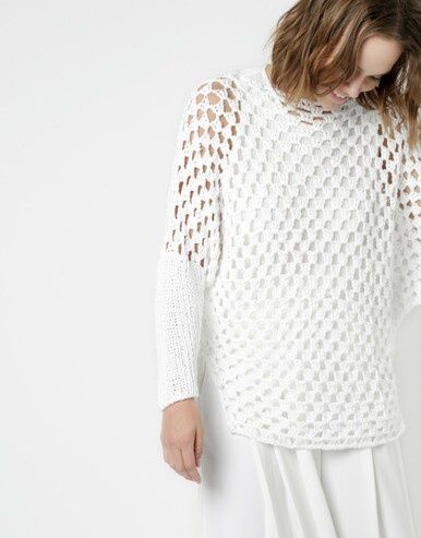 A woman is wearing a white crocheted sweater with knitted sleeves.