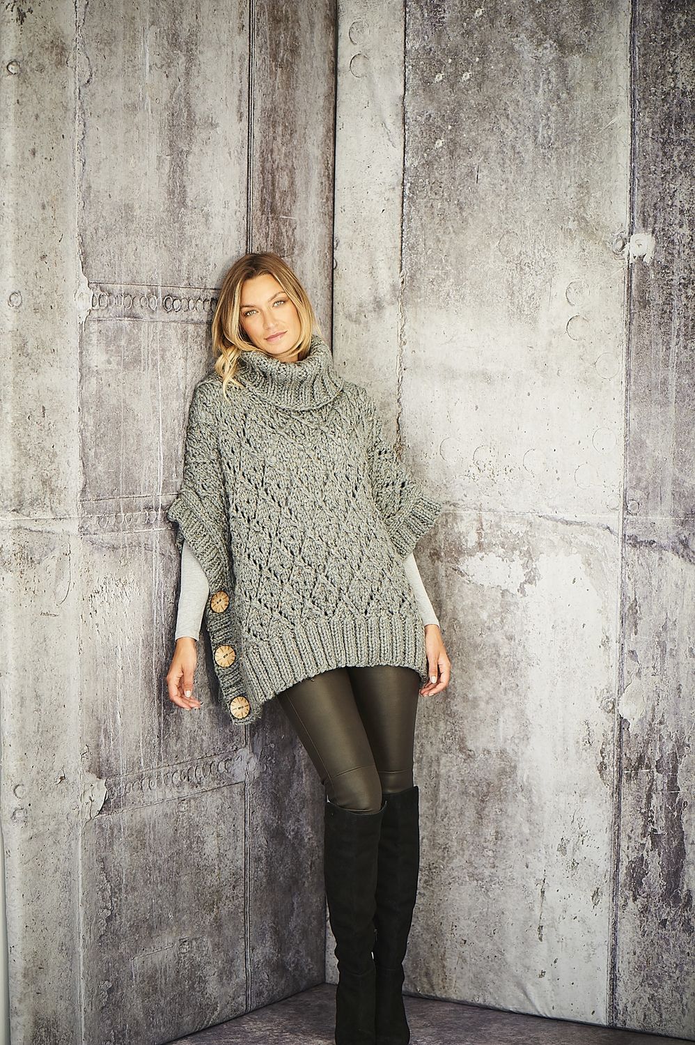 A woman is wearing a grey knitted poncho.
