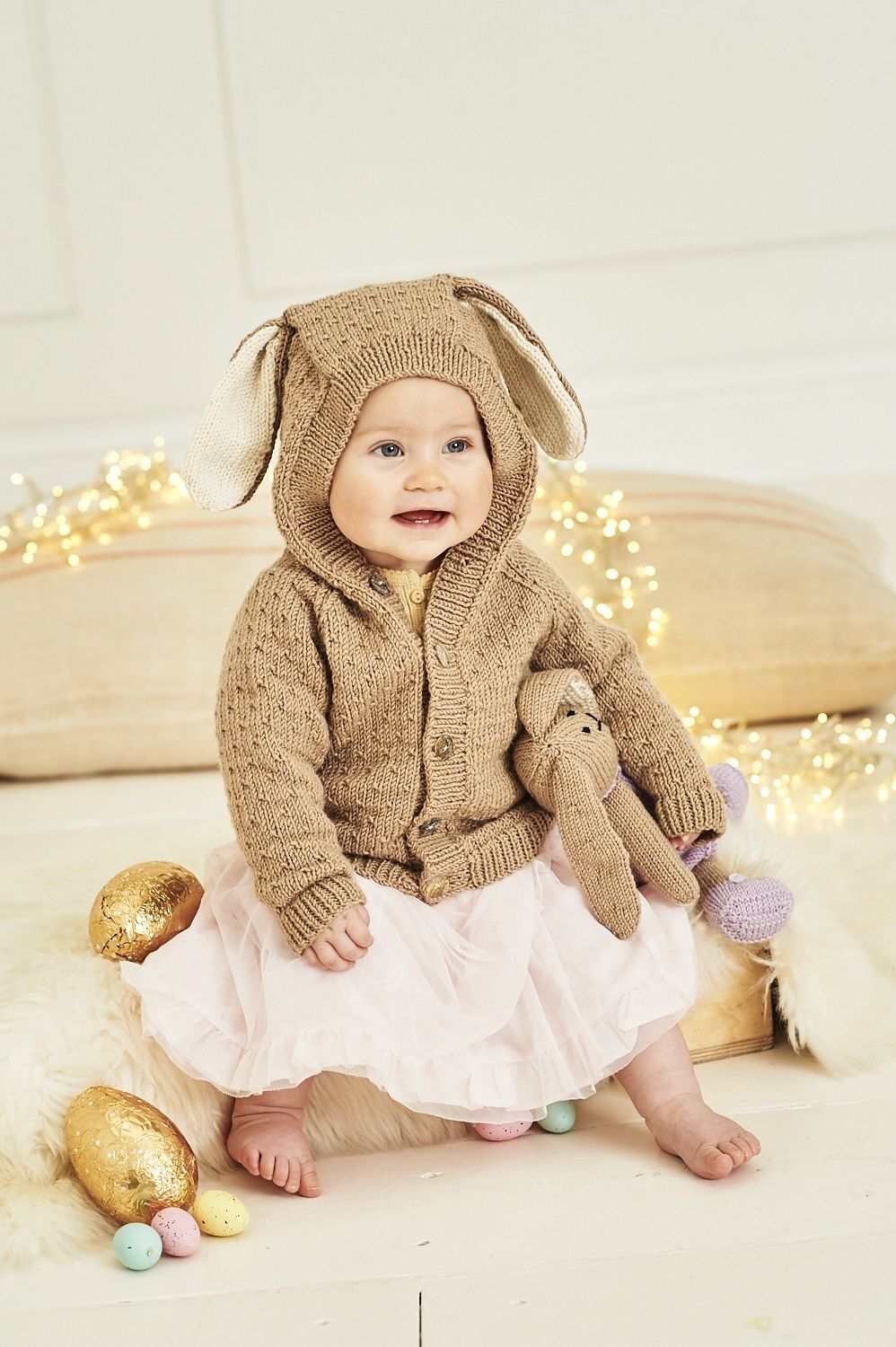 A baby is wearing a brown knitted cardigan to look like a bunny.