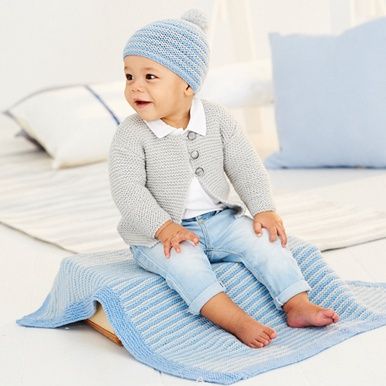A baby is sitting on a blue knitted blanket while wearing a grey knitted cardigan and a blue knitted hat.