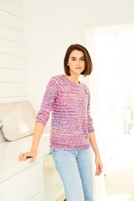 A woman is wearing a knitted sweater in a variegated pink and blue yarn.
