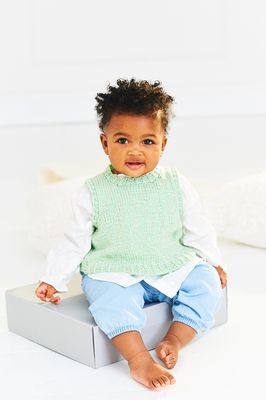 A baby is wearing a knitted green tank top.