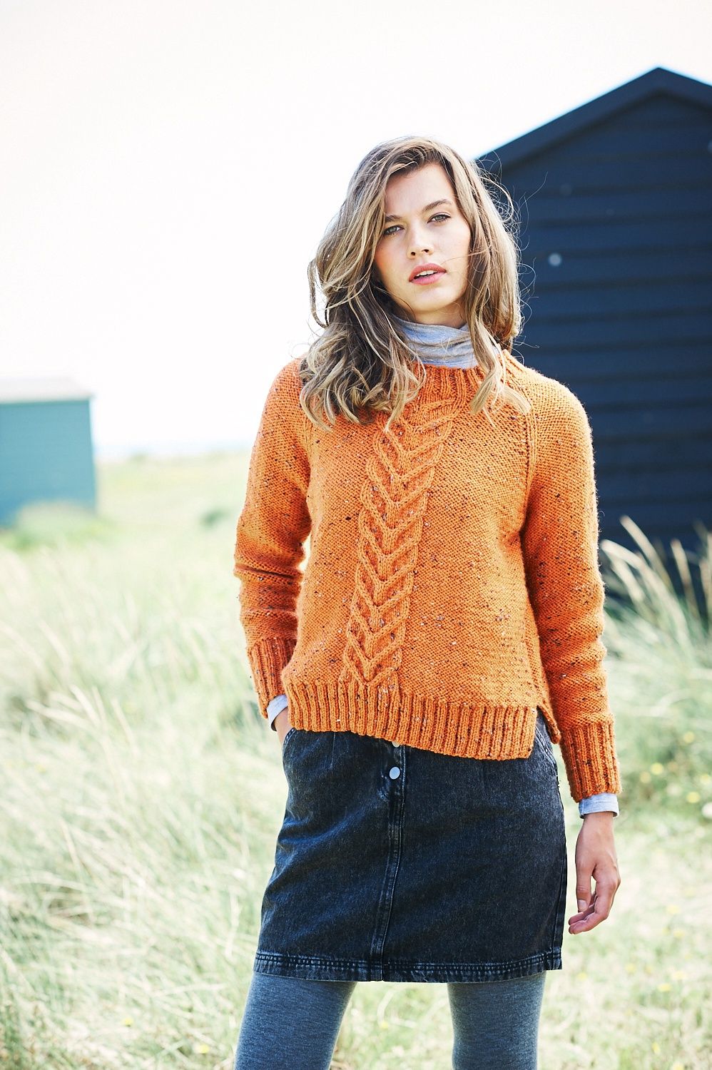 A woman is wearing an orange knitted sweater with cable down the front centre.