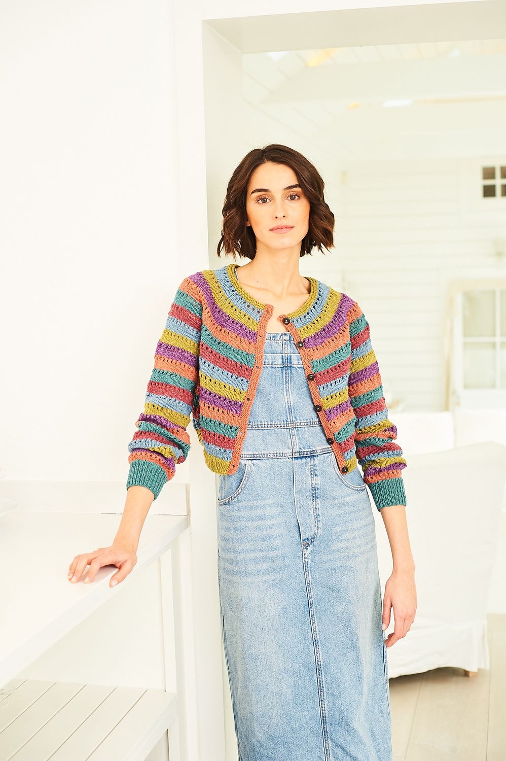 A woman is wearing a striped knitted cardigan in shades of green, blue, pink, purple, teal and orange.