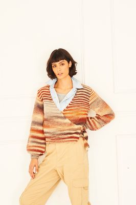 A woman is wearing a knitted cardigan in shades of cream, brown, red and orange.