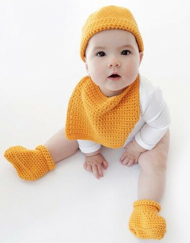 A baby is wearing an orange crocheted hat, bib and bootees.