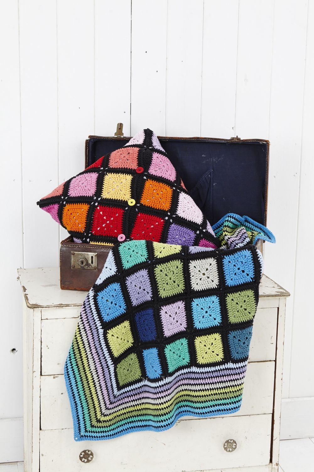 A crocheted blanket and cushion made of squares in every colour and joined with black.