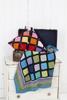A crocheted blanket and cushion made of squares in every colour and joined with black.