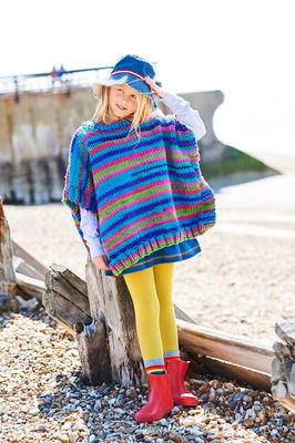 A girl is wearing a variegated knitted poncho in shades of blue, green and purple.