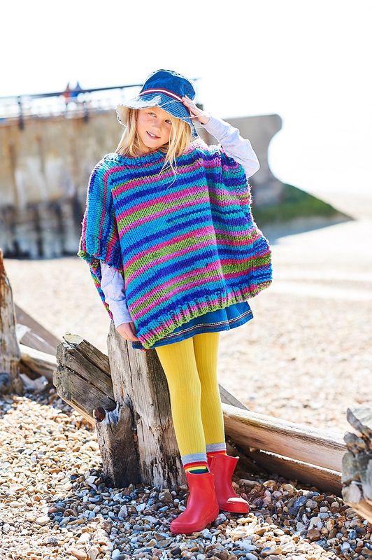 A girl is wearing a variegated knitted poncho in shades of blue, green and purple.